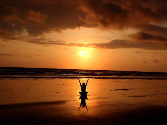 A woman sitting on the beach under a sunset learning how to heal spiritually.