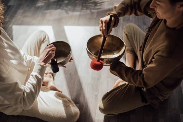 Two people sitting on the floor with sound bowls visiting one of the healing centers.