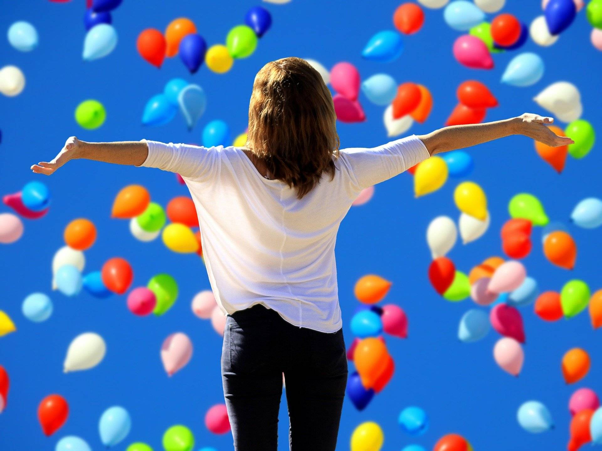 Woman standing in dropping balloons with her arms out after she read spiritual healing testimonials.