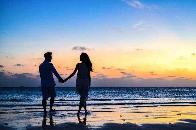 A couple on the beach holding hands who just did a love compatibility check.