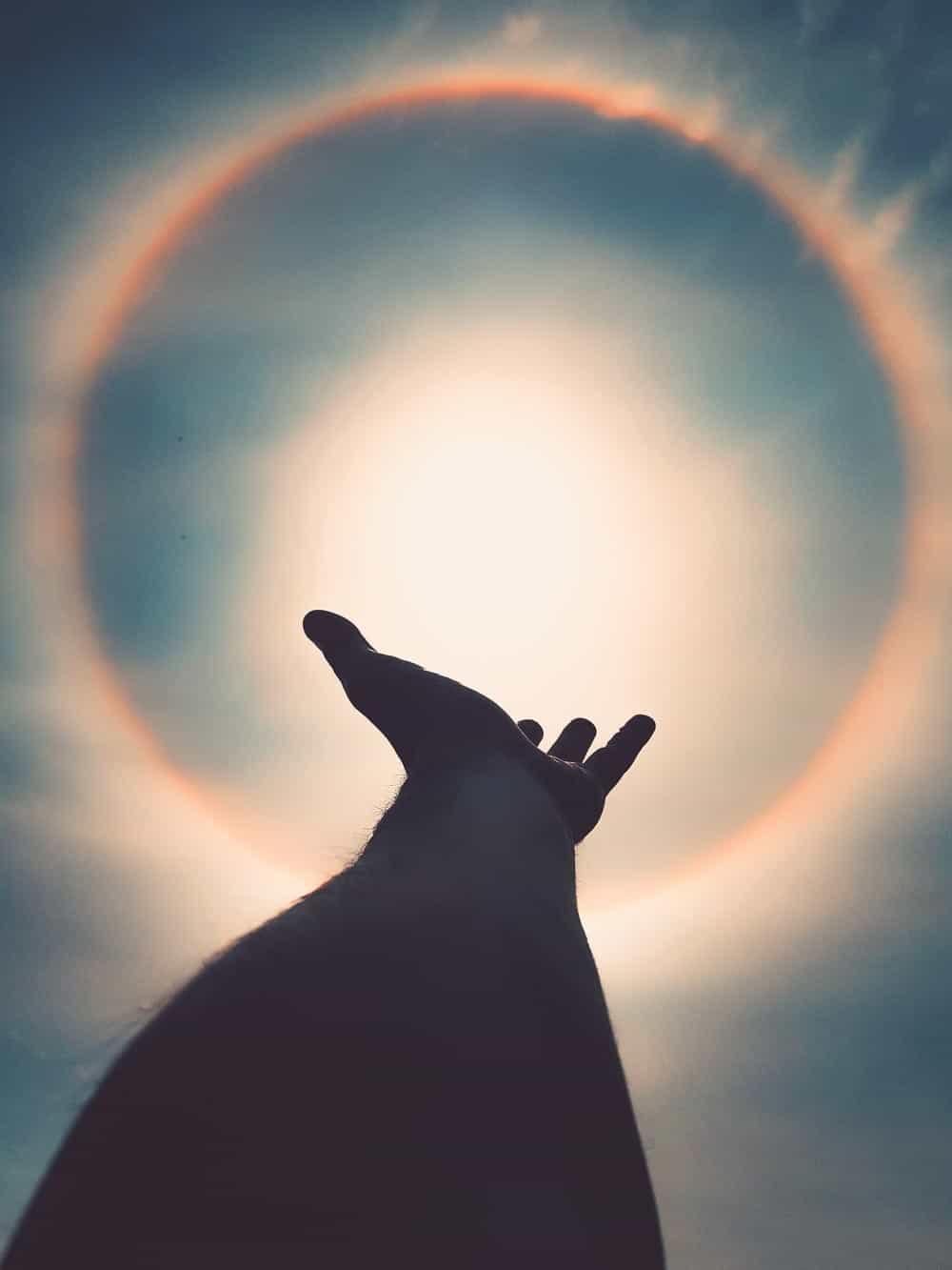 A arm of a person with real possession pointing up to the sky to a eclipse sun.